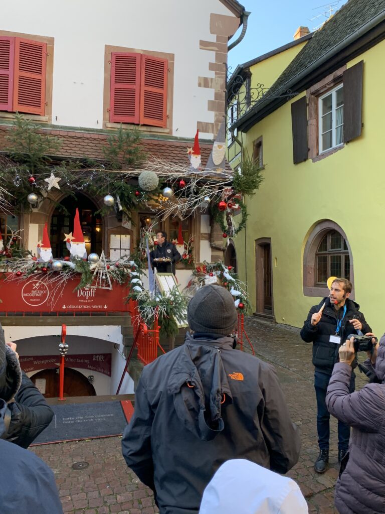 Guide speaking to guests outside a festively decorated wine cellar in a European Christmas market village on wellness river cruises
